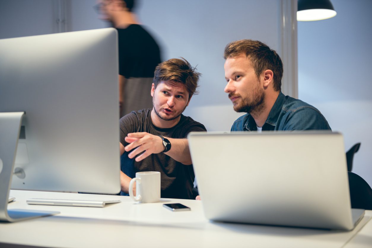 Two men sitting behind computers working together